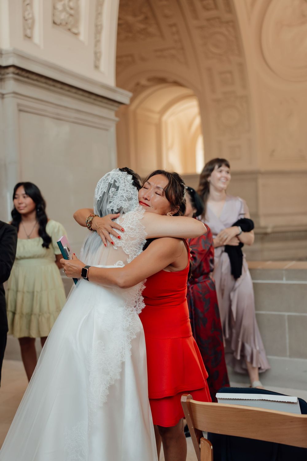 Wedding party members in colorful dresses share emotional embraces during reception celebrations.
