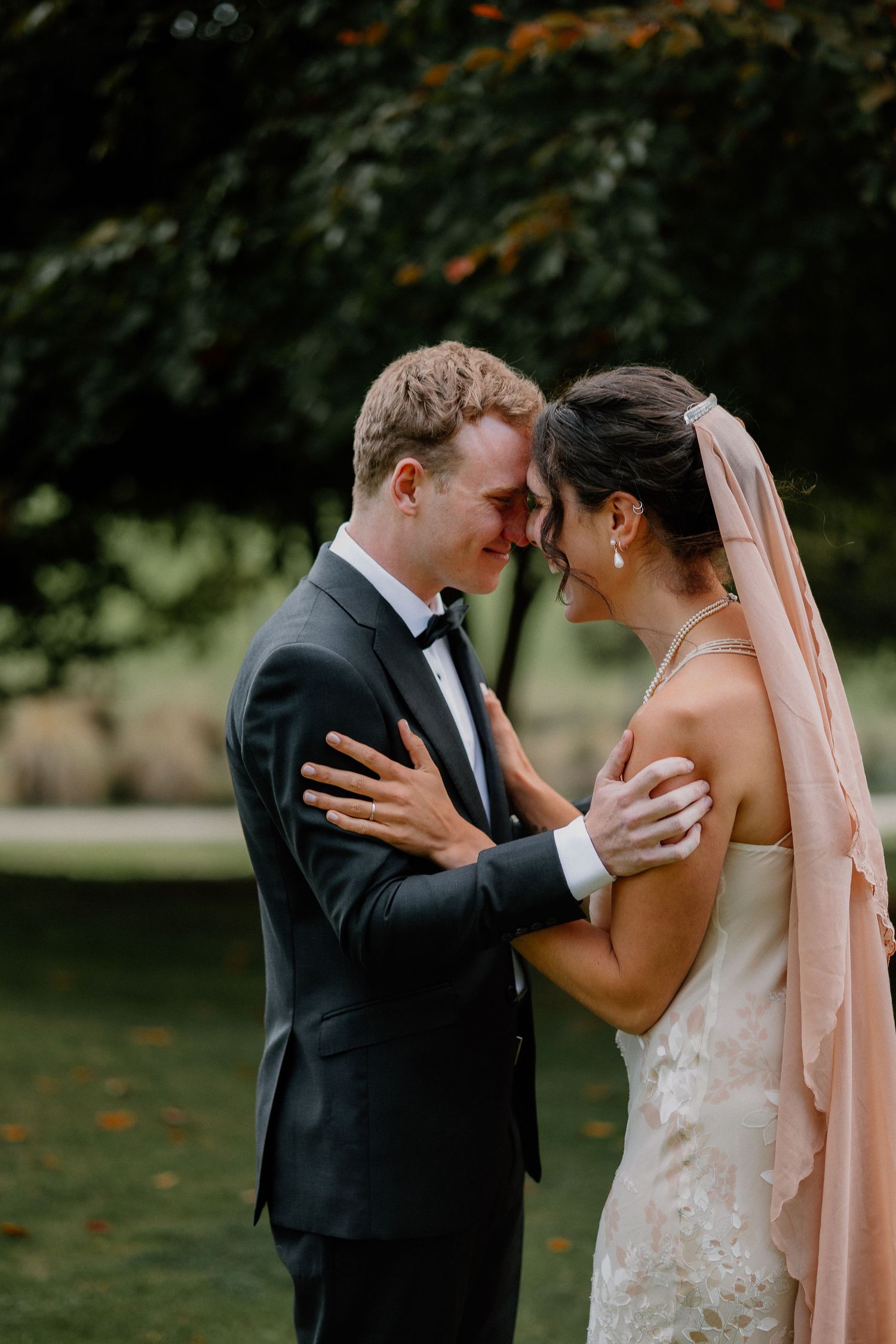 A romantic wedding couple shares an intimate embrace while dancing outdoors in a garden setting.