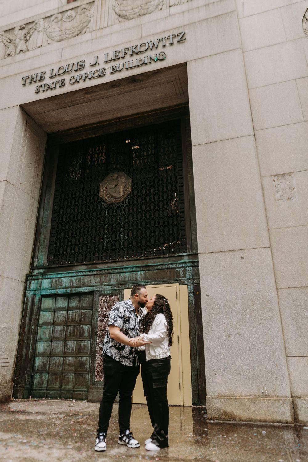 A romantic couple shares tender moments against an urban building facade with vintage architectural details.