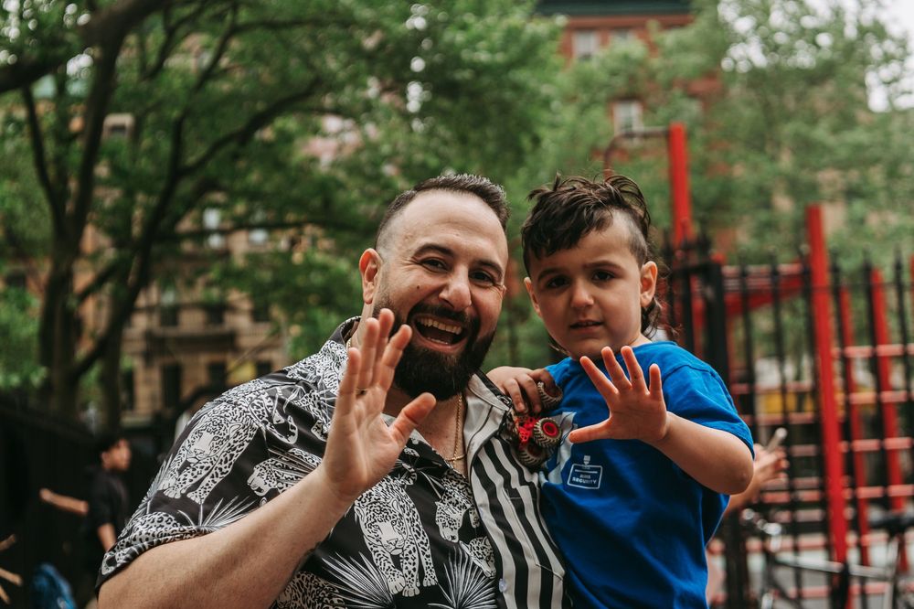 Two people in a park playfully pose and make heart shapes with their hands against a playground background.