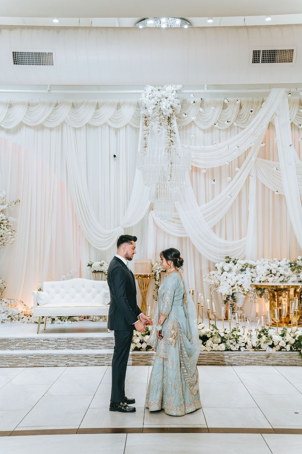Elegant wedding ceremony setup with white draping, floral arrangements and a couple in formal attire.