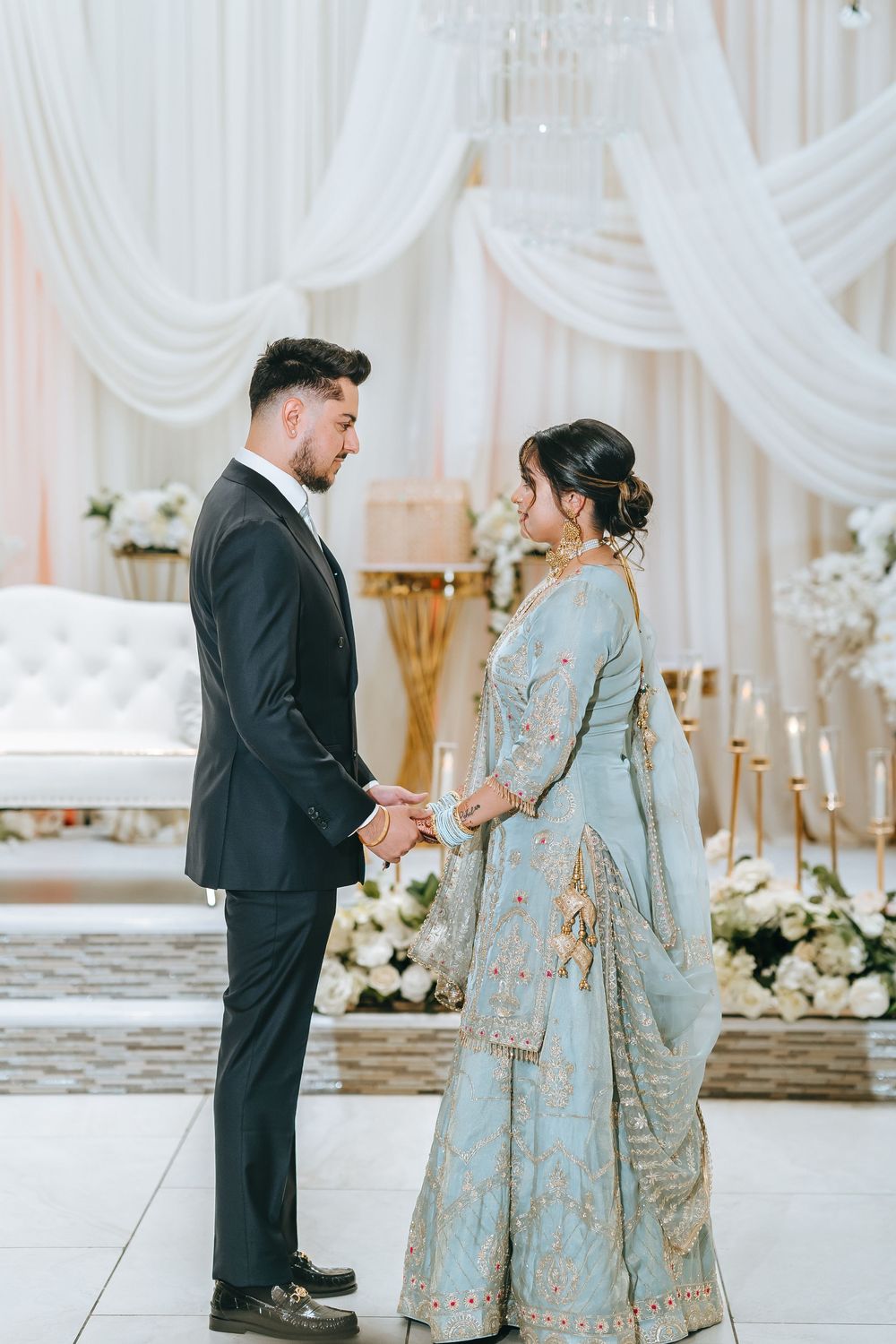 A couple in formal wedding attire having a private moment in front of white draped backdrop.