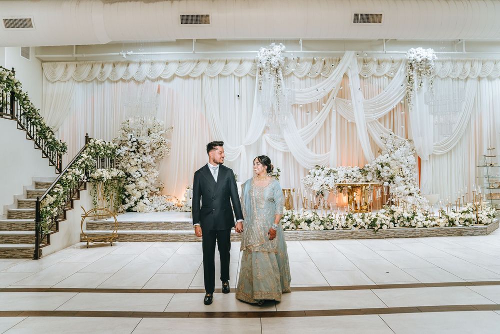 Wide shot of a wedding venue with white draping, floral arrangements and a couple in formal attire.