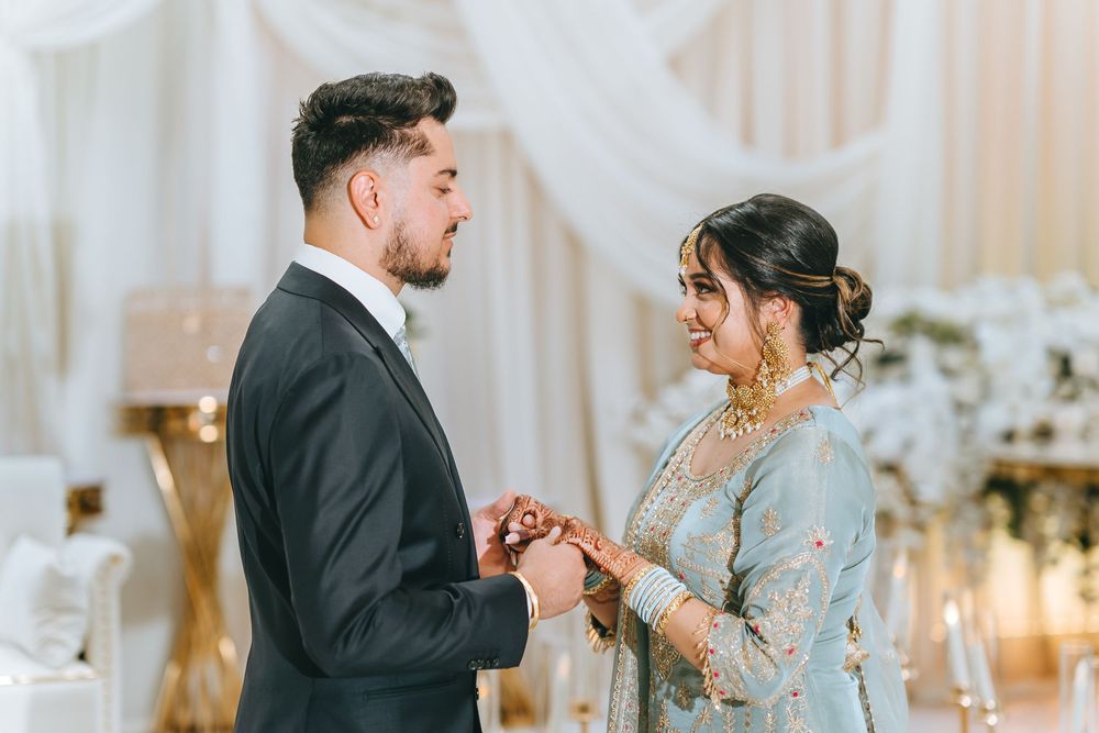 A couple exchanges rings during their wedding ceremony in front of an elegant white backdrop.