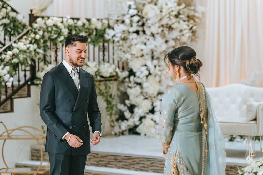 A couple in traditional wedding attire share an intimate moment in an elegantly decorated white reception hall.