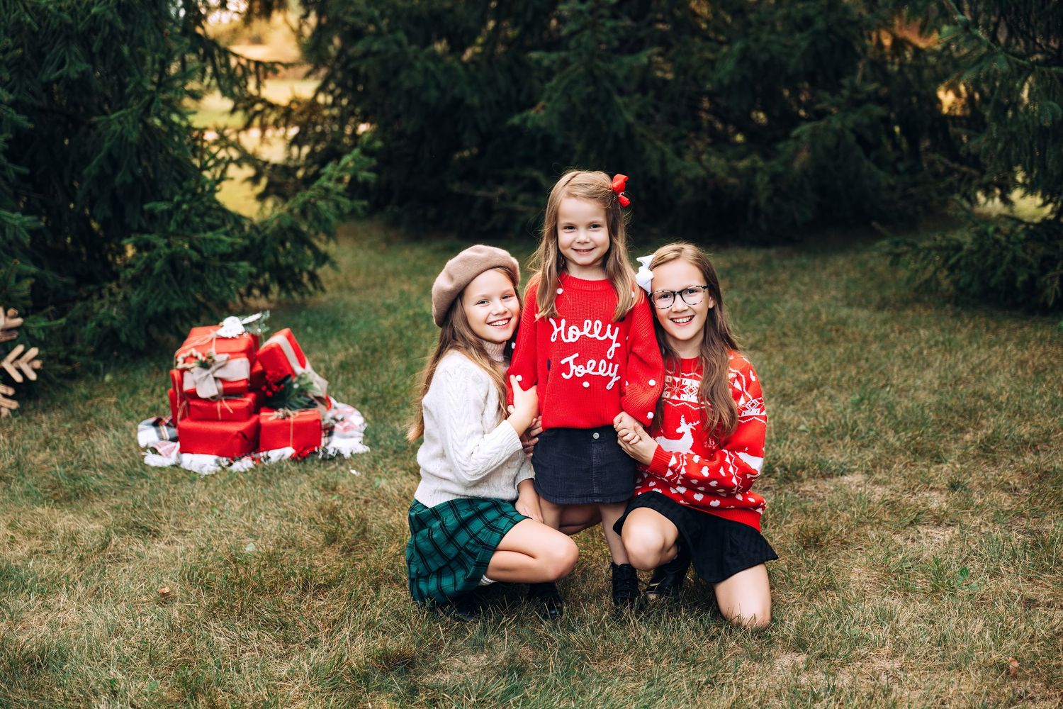 Three kids in Christmas sweaters with pine trees and presents in the background, hugging and laughing . Huntley, IL