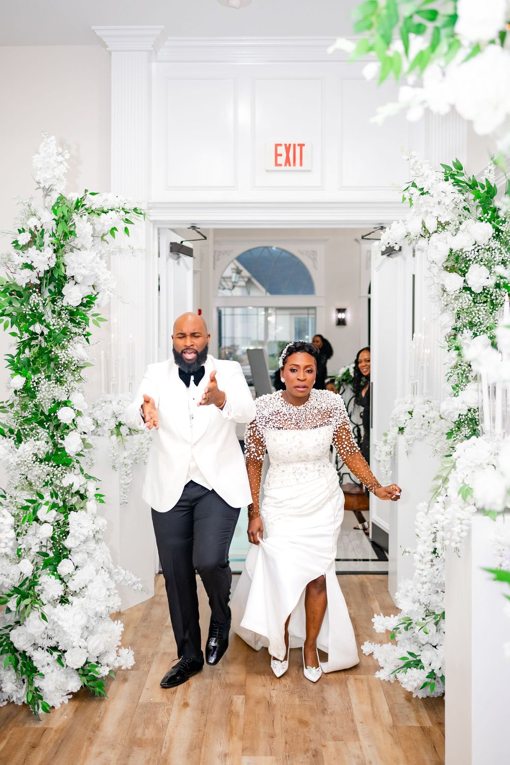 Wedding guests dance and celebrate on a wooden dance floor decorated with elegant white floral arrangements and greenery.