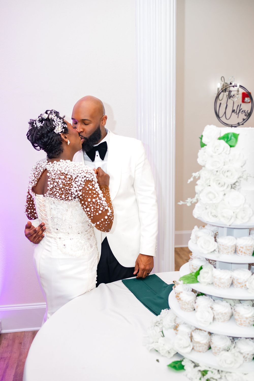 A tiered white wedding cake stands elegantly as a couple shares an intimate moment during their reception celebration.