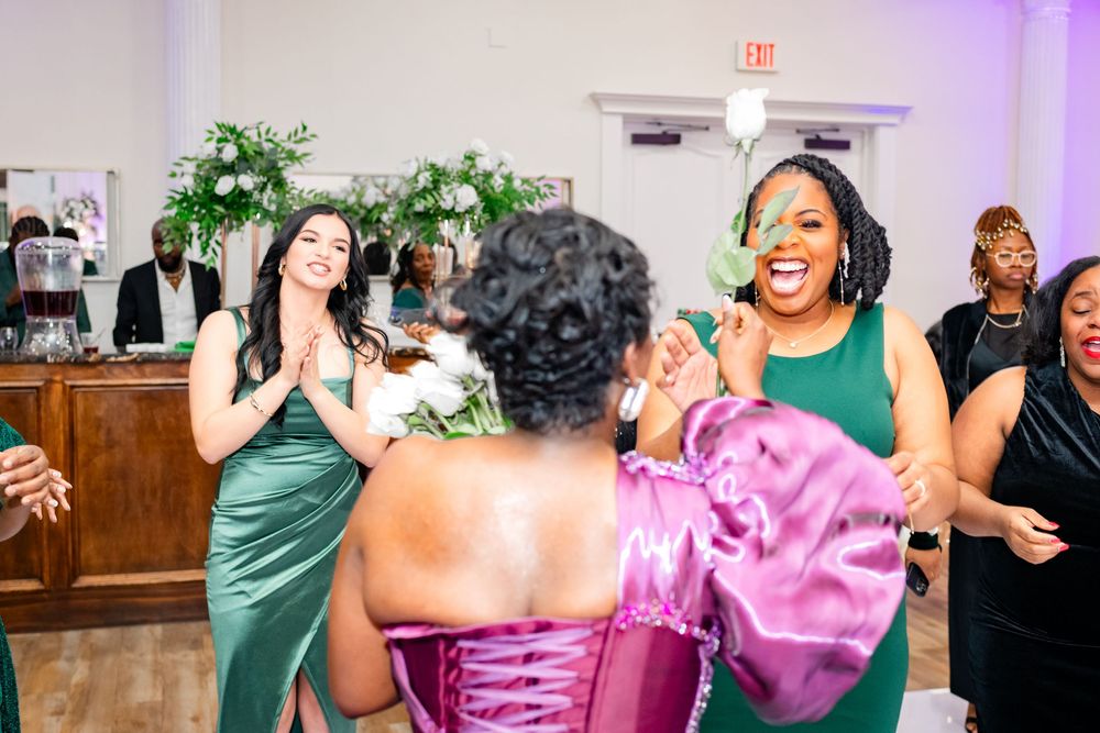 A group of wedding guests dance and celebrate together on a dance floor with purple lighting effects.