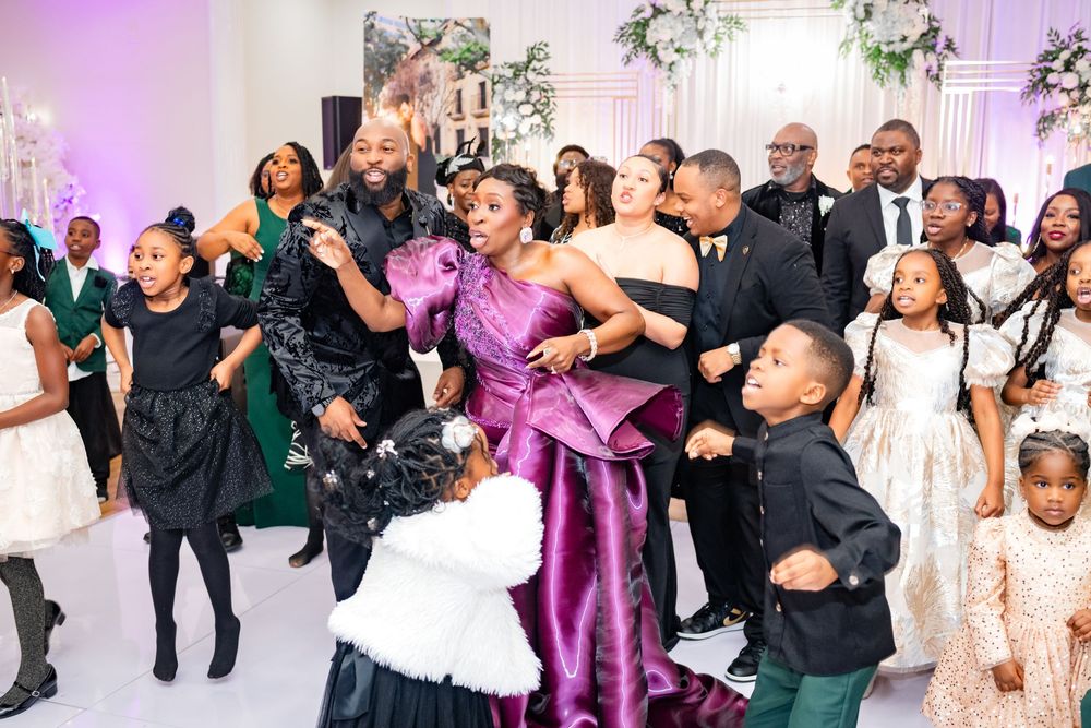 Wedding guests dance and celebrate together on a dance floor illuminated with purple lighting at a reception party.