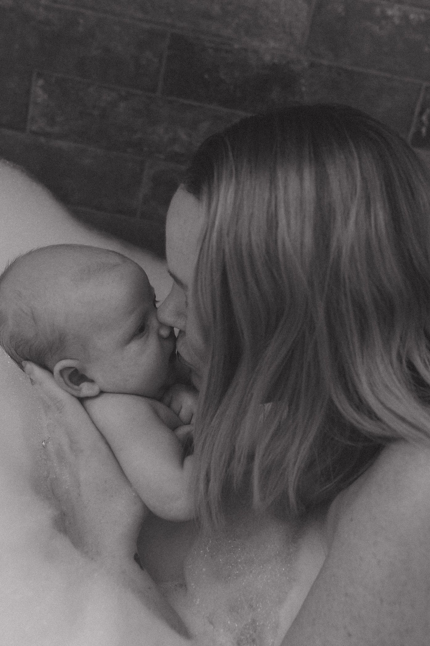 A tender black and white portrait showing an intimate bonding moment between parent and baby.