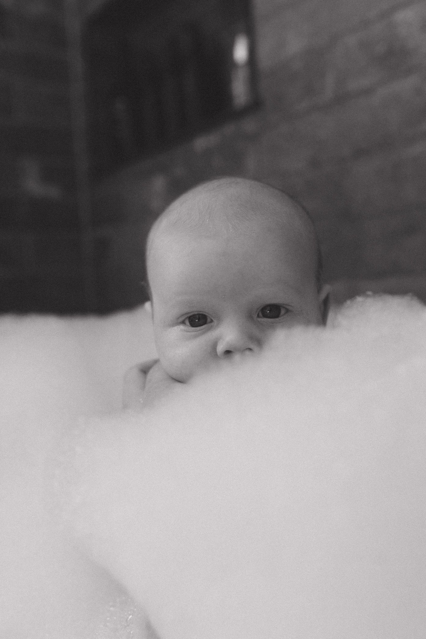 Close-up black and white portrait showing eyes peeking above soft white fabric or bedding.