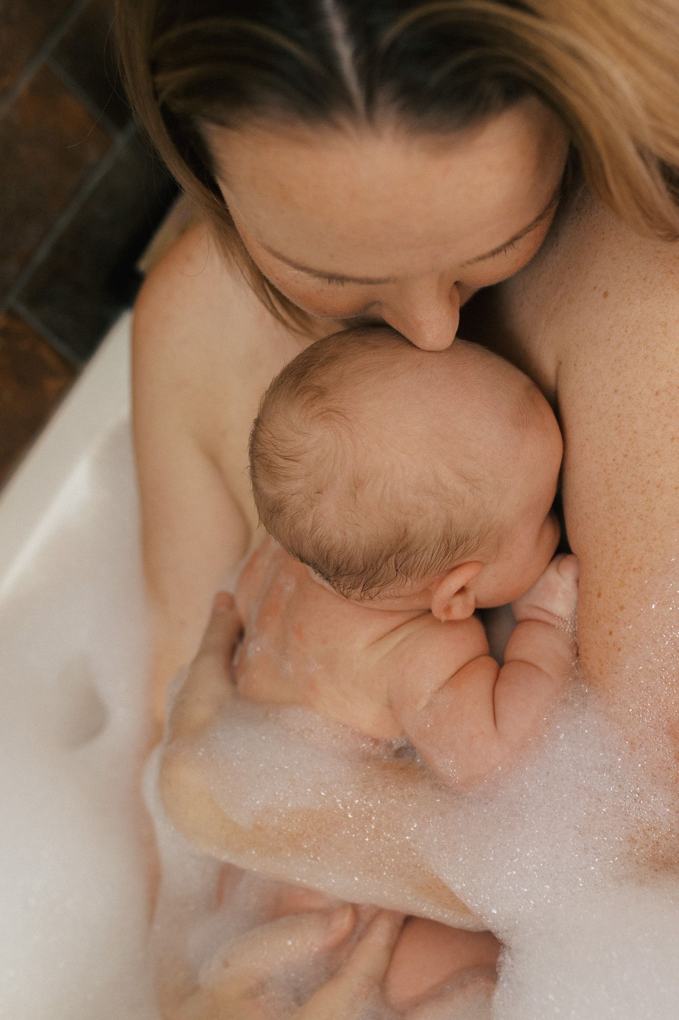 Tender bathtime moment showing parent and baby in soapy bubbles.