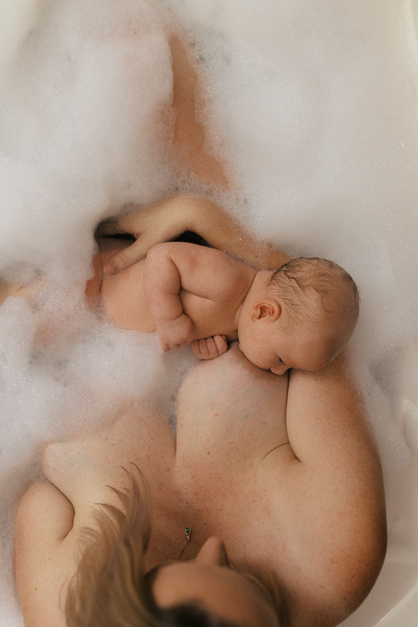 Baby taking a bath in soapy water with gentle bubbles surrounding their small body.