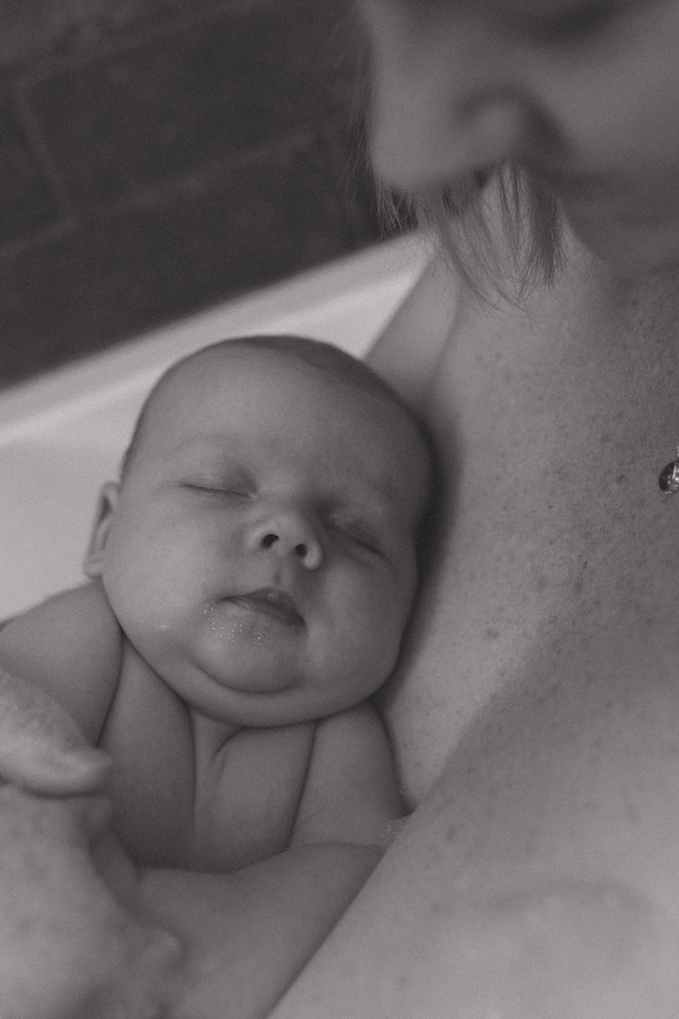 A peaceful black and white photograph showing a sleeping infant resting against soft fabric.