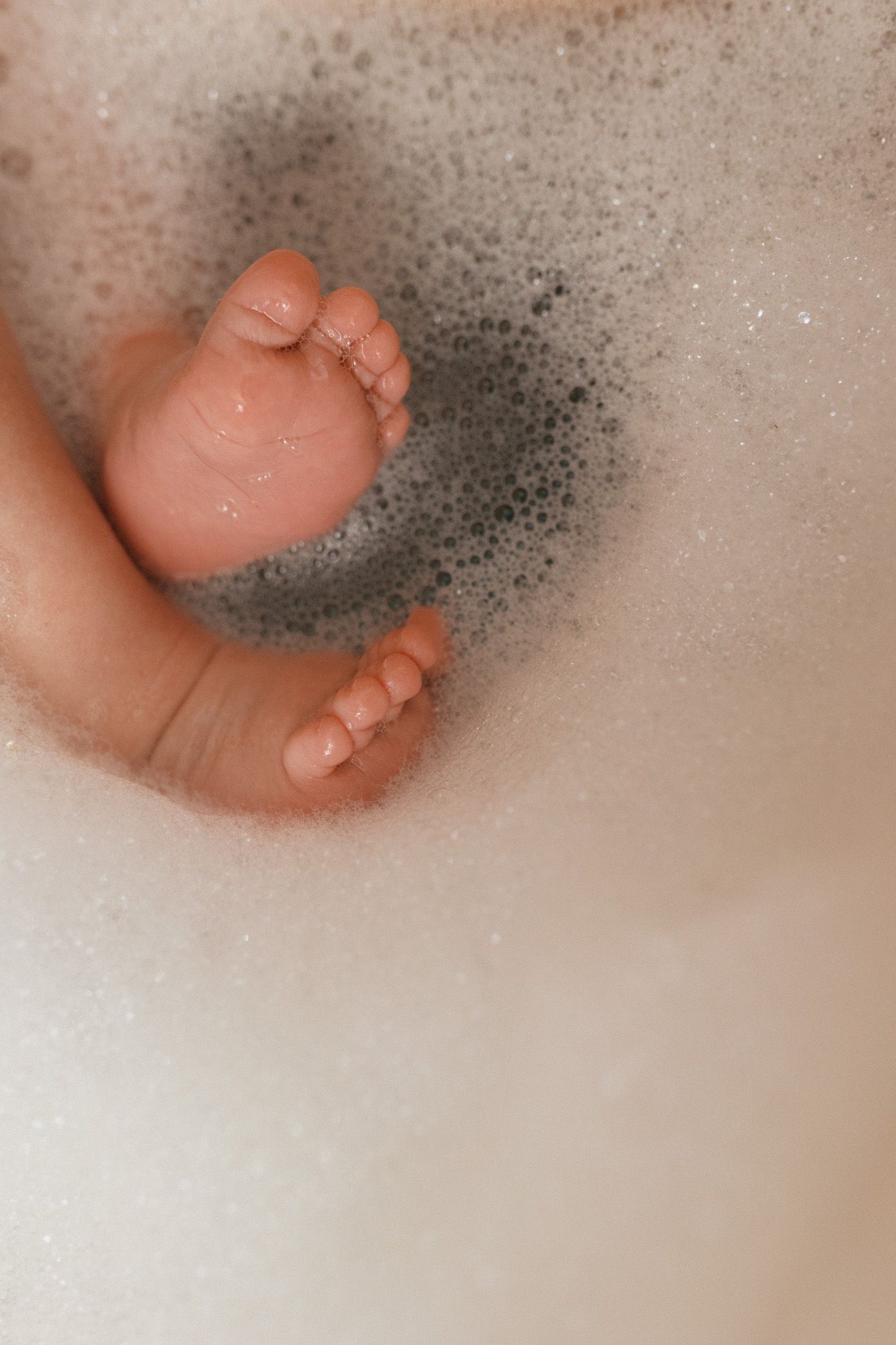 Close-up of tiny baby feet peeking through bath bubbles and foam.