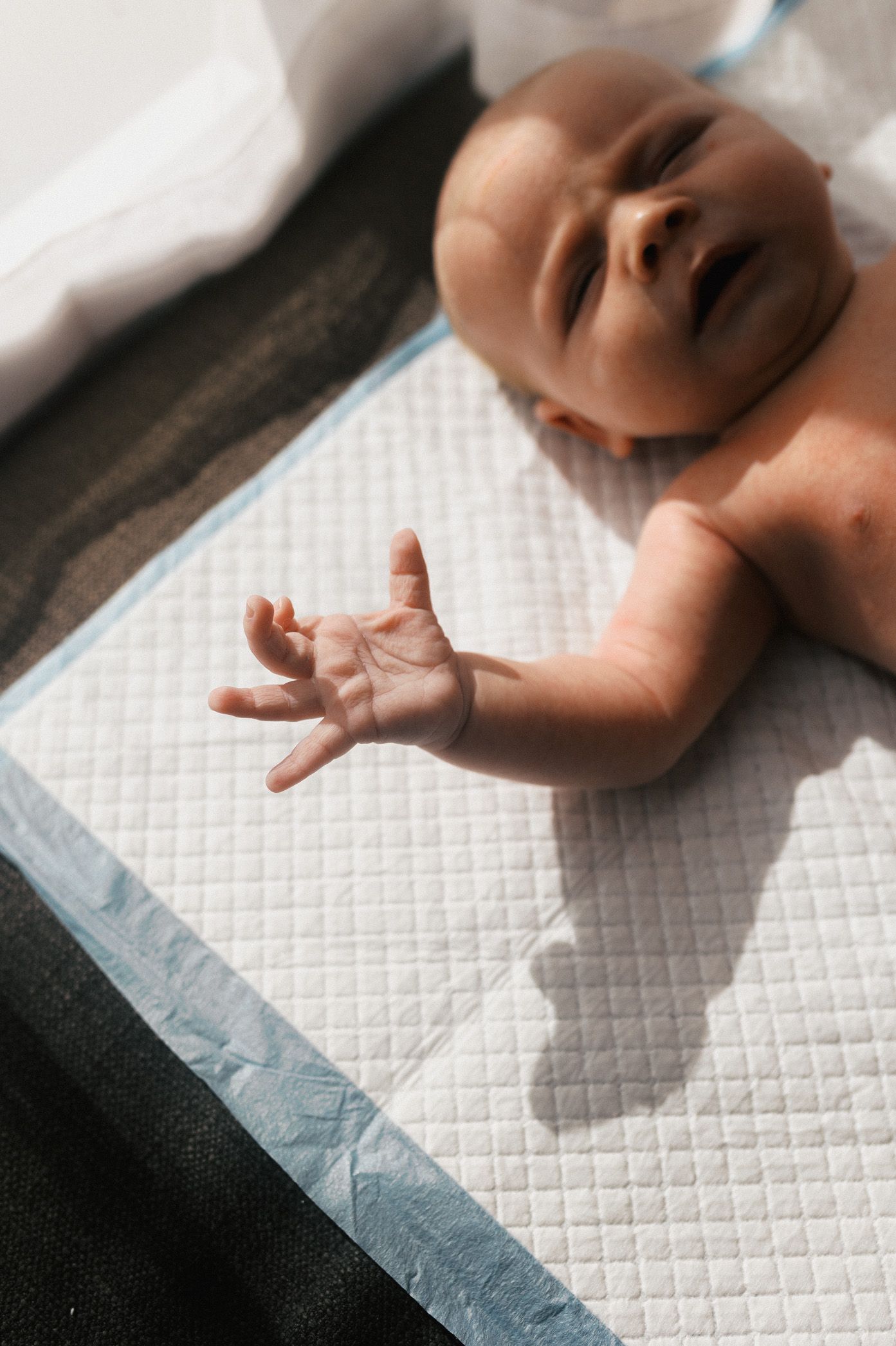 Baby's small hand casting shadow on textured white surface in natural light.