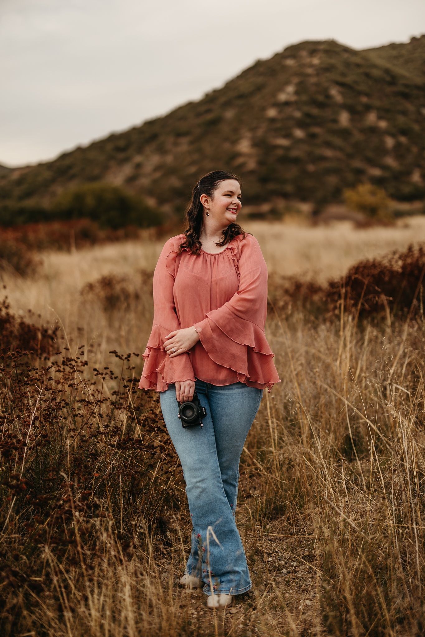 Woman smiling looking into the distance holding a camera.