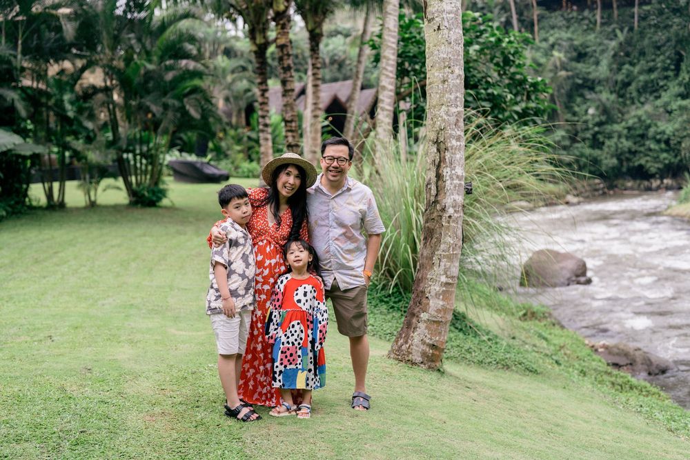 A family explores a lush tropical garden path with palm trees and greenery along a flowing stream.