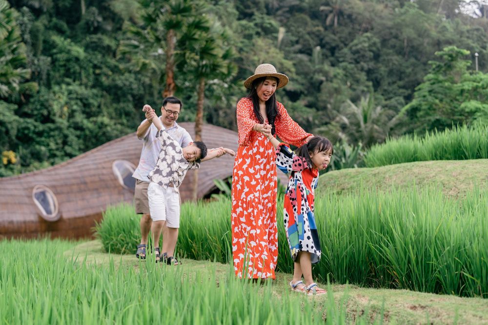 Tourists walking along lush green rice terraces and palm trees in tropical Bali countryside landscape.