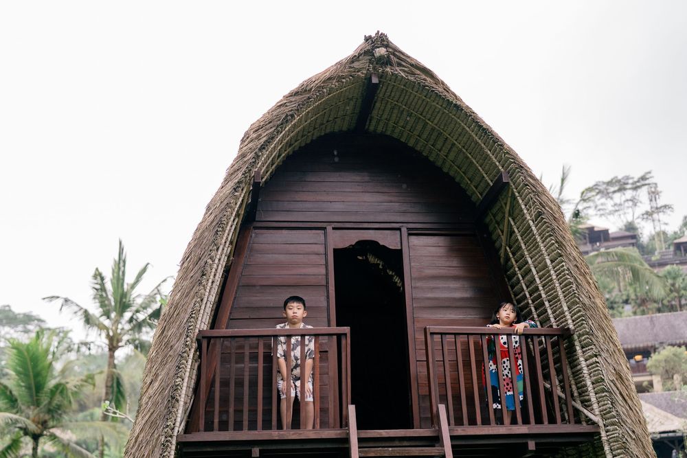 Traditional wooden bungalows with curved thatched roofs stand in a tropical resort setting with palm trees and greenery.