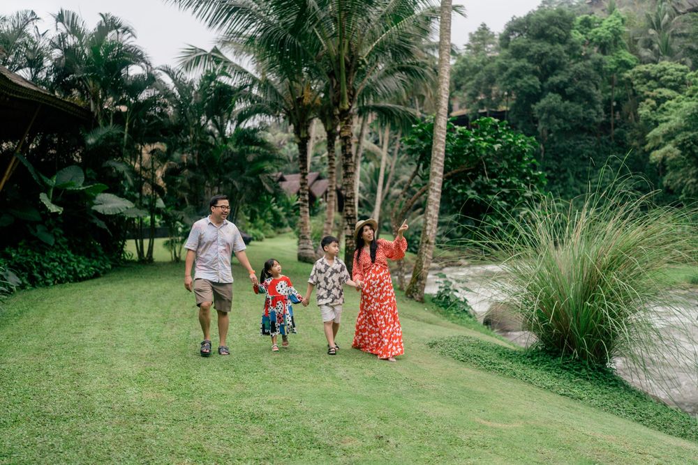 A family walks together along a lush tropical path lined with palm trees and greenery.