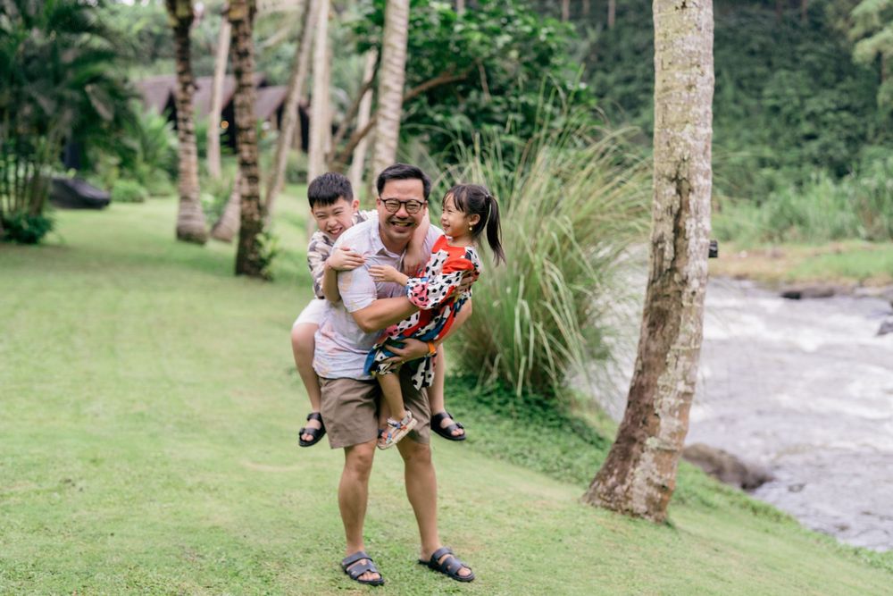 A group of people enjoying outdoor activities in a lush green park setting with palm trees and a stream.