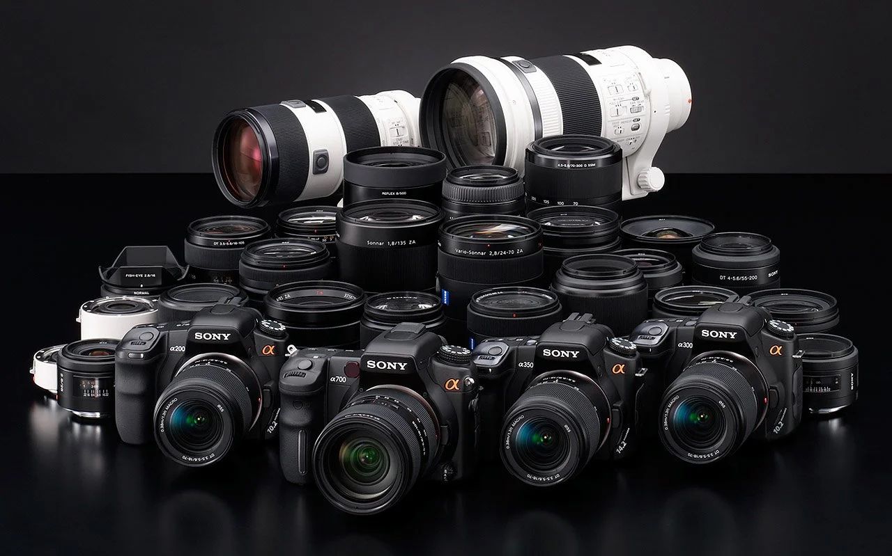 Sony Alpha series mirrorless digital cameras and interchangeable lenses displayed in a row against white background.
