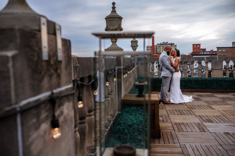 A romantic rooftop wedding venue decorated with string lights and vintage decor overlooking a cityscape at sunset.