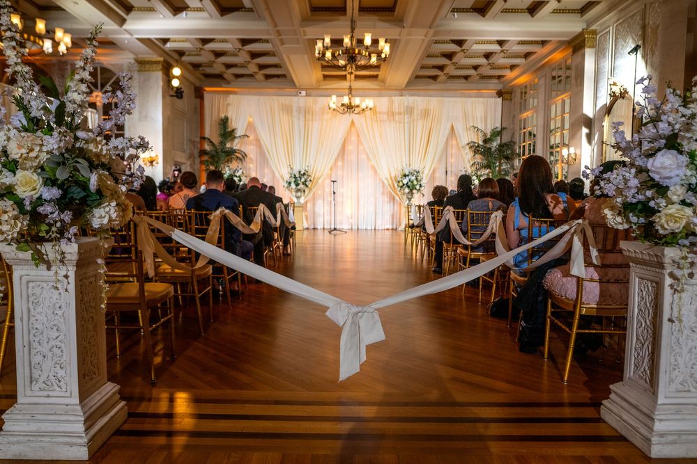 An elegant wedding ceremony space with white draping, floral arrangements, and wooden beams in an industrial venue.