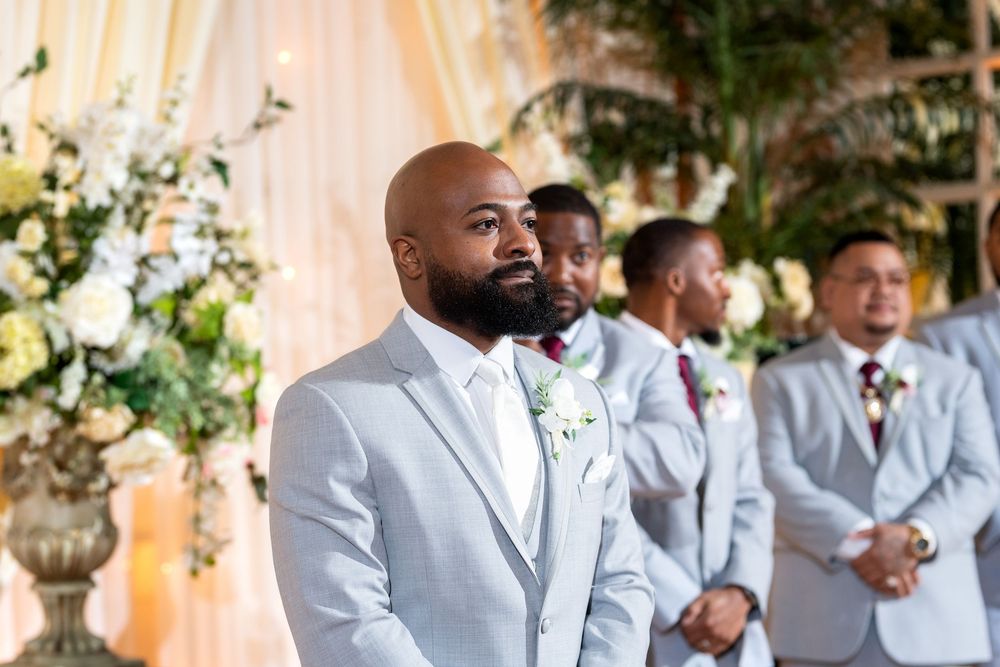 Wedding party members in light gray suits pose together during outdoor celebration.