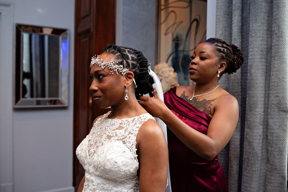 A bride in a white lace wedding dress and veil stands against a grey wall during a formal wedding ceremony.
