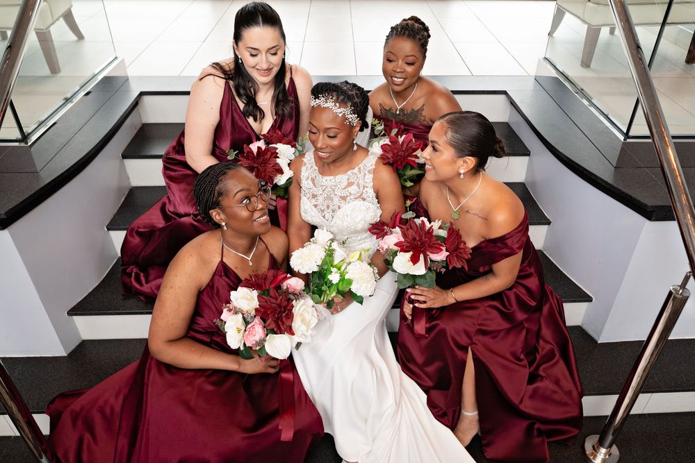 Bridal party in burgundy dresses and white wedding gown pose together in a modern venue.