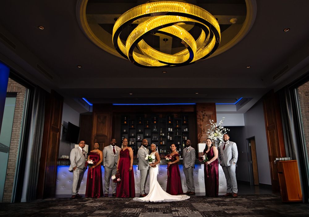 Wedding party members stand in a dramatic line against a dark background with warm lighting creating an elegant silhouette.