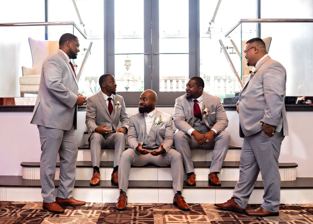 Group wearing matching gray suits sit on stairs in sequence of candid poses during wedding photoshoot.