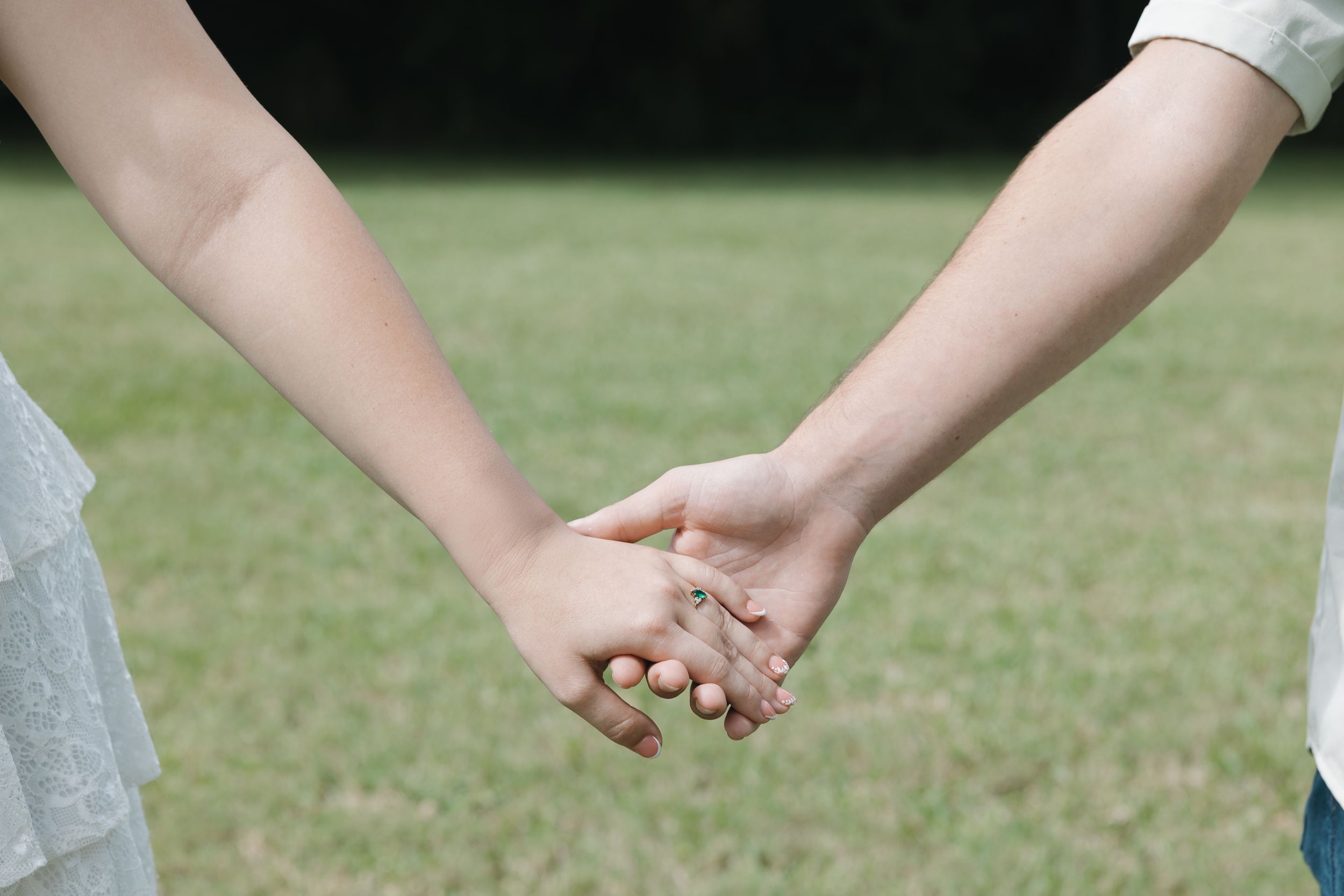 A couple's hands rest gently on each other in a romantic outdoor setting.