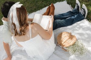 A romantic picnic scene with white blanket and straw accessories on green grass.