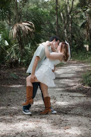 A romantic dip pose on a tree-lined path with brown boots and white dress.