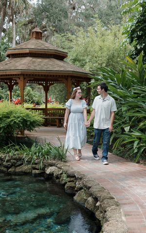 A romantic garden scene with a wooden gazebo surrounded by lush plants and a stone-lined pond.