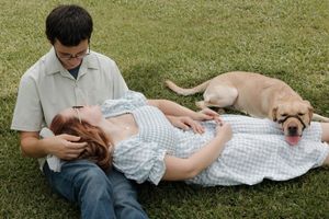 A couple relaxes on grass with their friendly Labrador dog on a sunny afternoon.