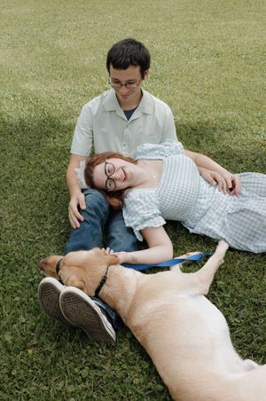A relaxed outdoor portrait on grass featuring a couple and their loyal Labrador companion.