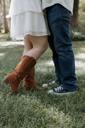 Brown cowboy boots and sneakers stand together on green grass, showing contrasting footwear styles.