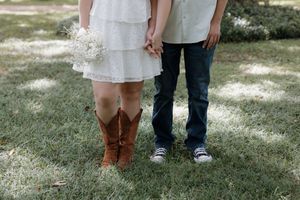 A close-up of brown cowboy boots and sneakers standing together on grass.