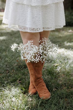 Brown suede boots adorned with delicate baby's breath flowers against a white lace dress.
