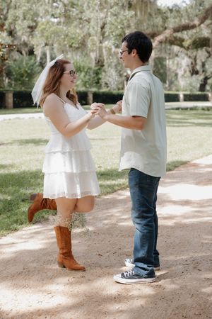 A couple dances playfully on a dirt path surrounded by trees and greenery.