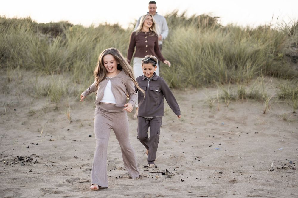 A couple walks together through coastal sand dunes on a romantic beach engagement photoshoot.