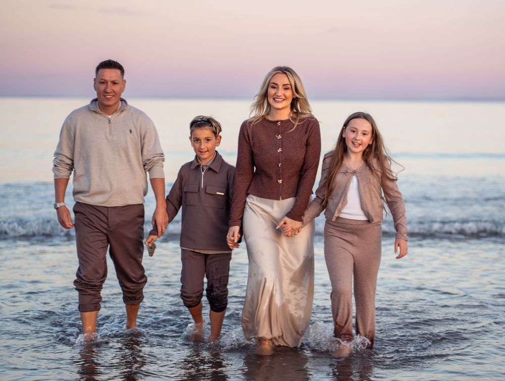 Group standing in shallow ocean water at sunset wearing coordinated brown and beige outfits.