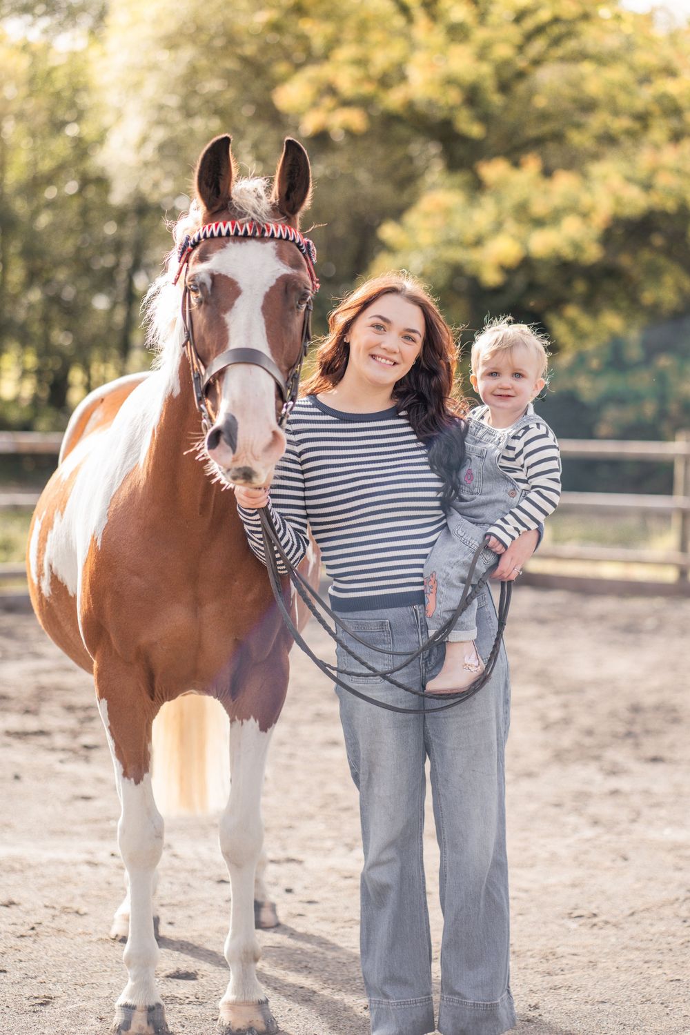 A brown and white horse stands with people in a sunny outdoor paddock wearing matching striped shirts.
