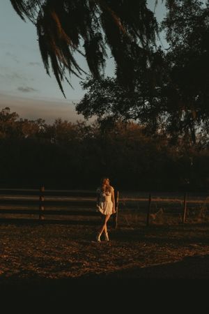 Golden hour lighting illuminates a rustic farm field with figures walking near a wooden fence.
