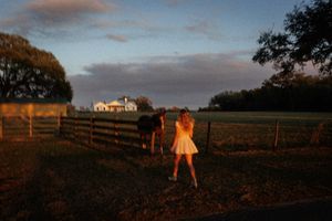 Sunset landscape with wooden fences and a farmhouse in the distance.